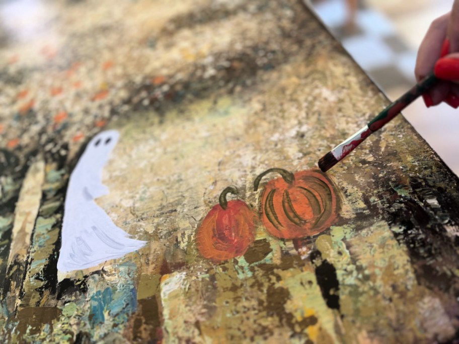 painting pumpkins on a thrift store canvas painting for halloween