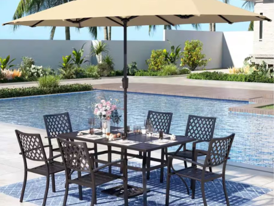 an outdoor dining table set with an umbrella by a swimming pool
