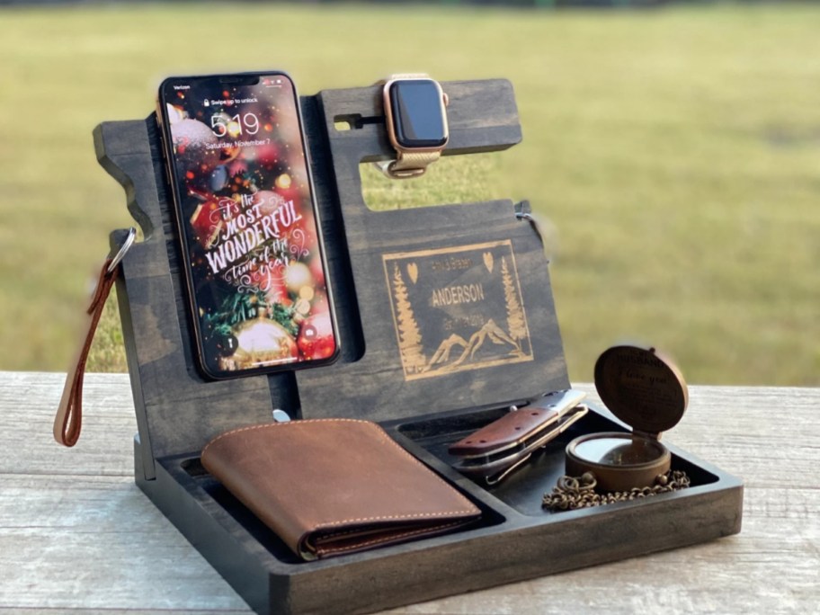 a wood docking station with a phone, watch, wallet, sunglasses on it