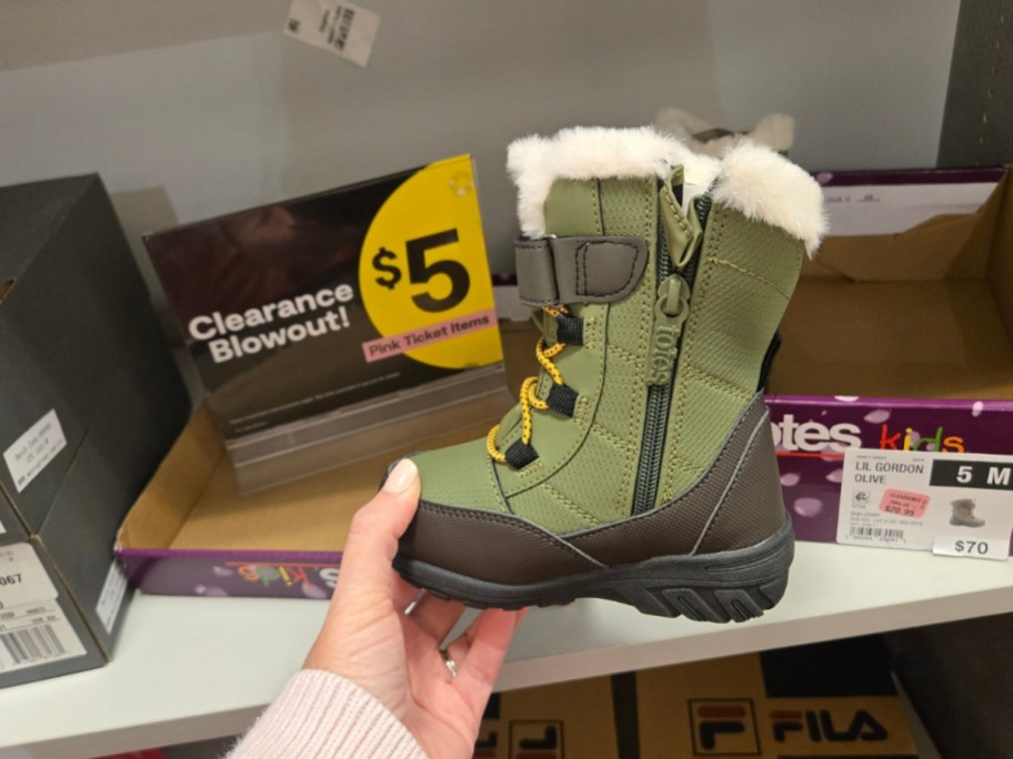 hand holding a kids winter boot in front of a clearance sign on a store shelf