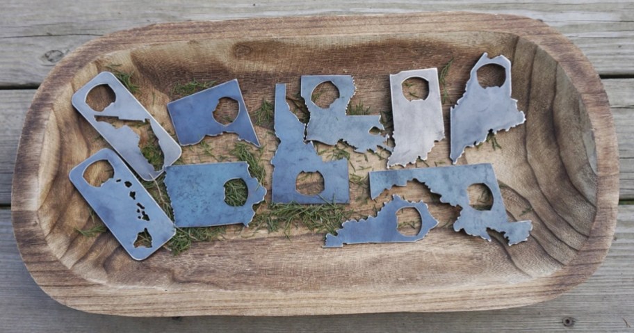 a wood bowl with steel US State shaped bottle openers