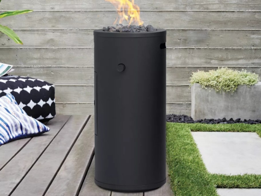 a black round column style firepit in a backyard