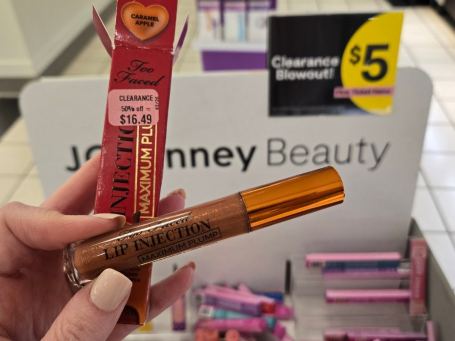 hand holding a tube of Too Faced Lip Injector in front of a clearance sign in a store