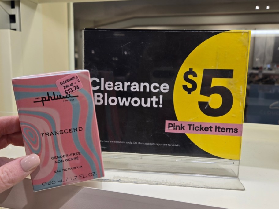 hand holding a box of perfume in front of a clearance sign in a store