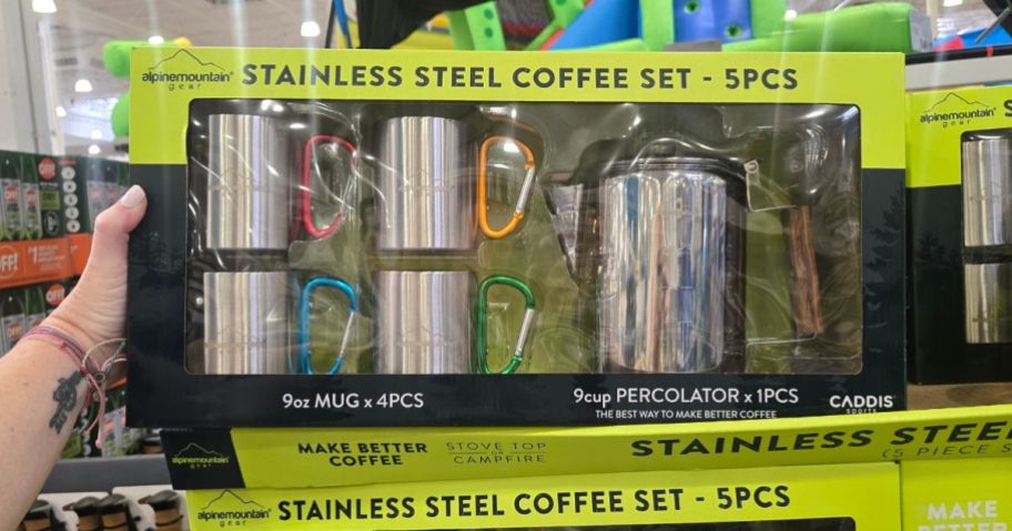 A person holding a set of stainless-steel coffee mugs and a kettle