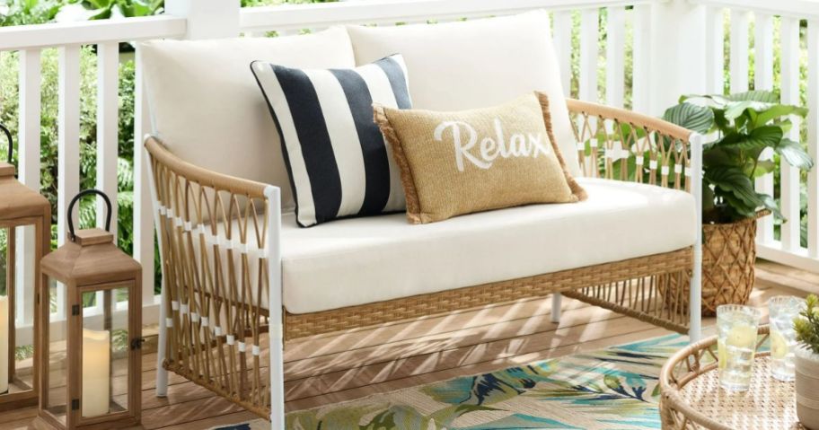 A wicker loveseat with pillows on it 