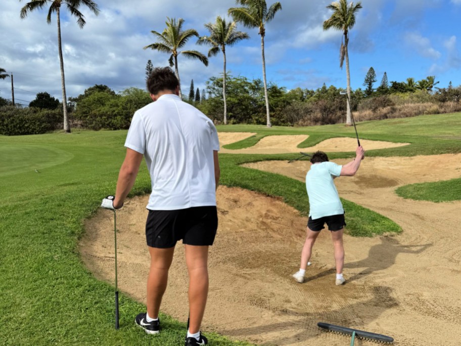 Two boys golfing surrounded by palm trees