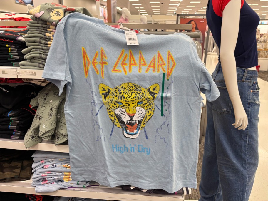 Light blue Def Leppard band T-shirt at Target featuring a roaring leopard graphic and “High ’n’ Dry” text, displayed on a store rack.