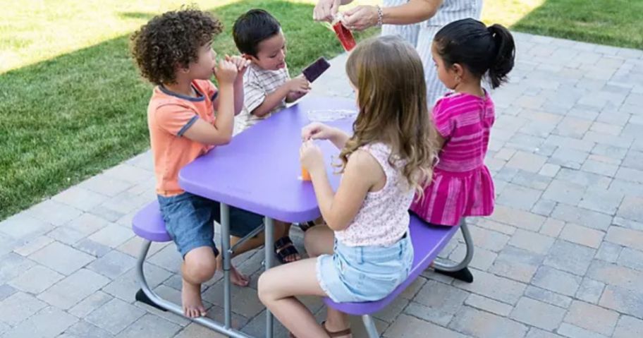 4 kids sitting on a Lifetime Folding Children's Picnic Table eating popsicles outside