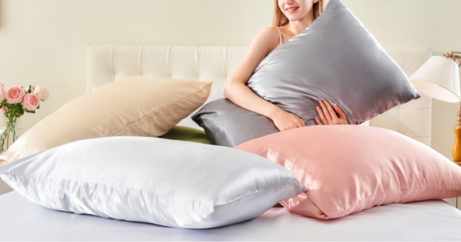 a woman sitting on a bed with pillows in various colors of satin pillowcases