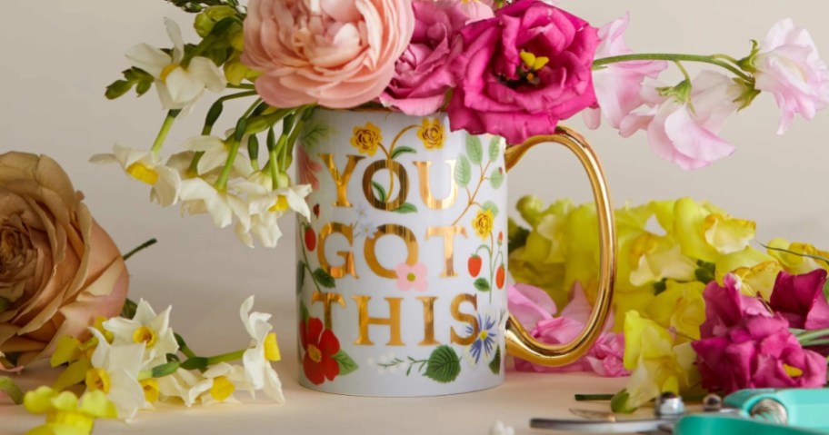 a floral and gold coffee mug that says "You Got This" filled with flowers and more flowers on a table around it