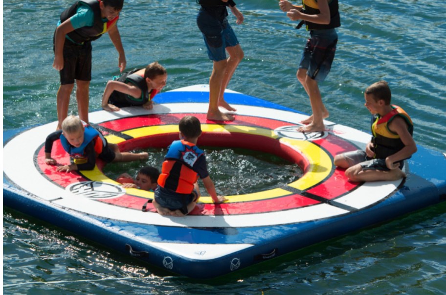bunch of kids in the middle of a lake playing on a large water pad