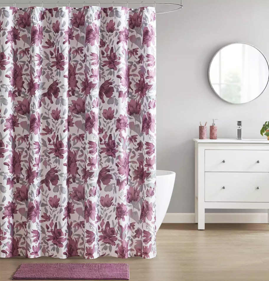 bathroom with a purple floral print shower curtain, coordinating bath rug, and vanity with lotion and soap pumps