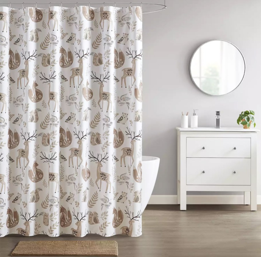 bathroom with a woodland print shower curtain, coordinating bath rug, and vanity with lotion and soap pumps