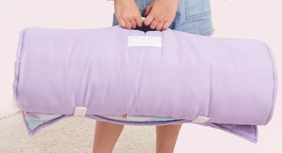 hand holding a purple rolled up nap mat via its handles 