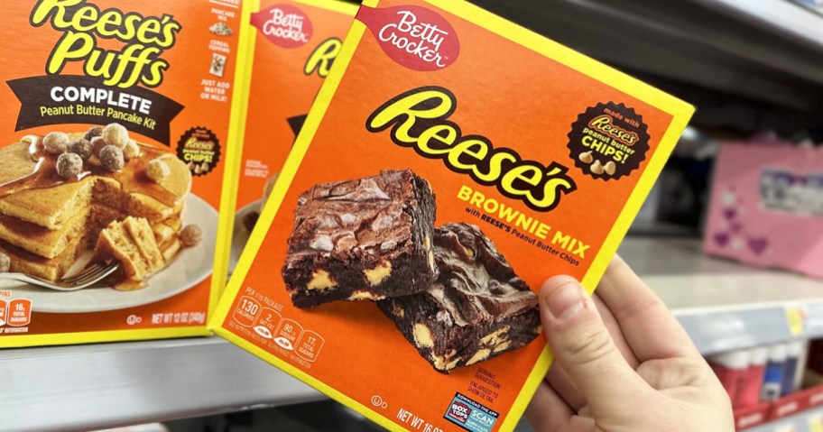 hand grabbing an orange box of Reese's Brownie Mix from store shelf