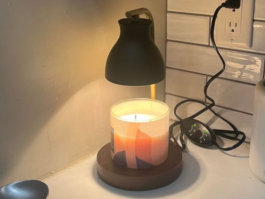 A candle in a warmer lamp on a counter