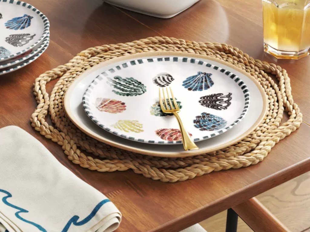 Rattan charger plates on table top with seashell, stoneware plate, and fork on to