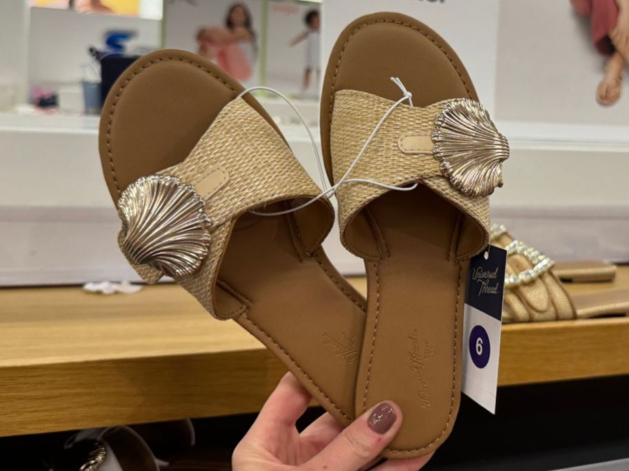 Hand holding a pair of Universal Thread Women's Nesryn Raffia Shell Ornament Slide Sandals 