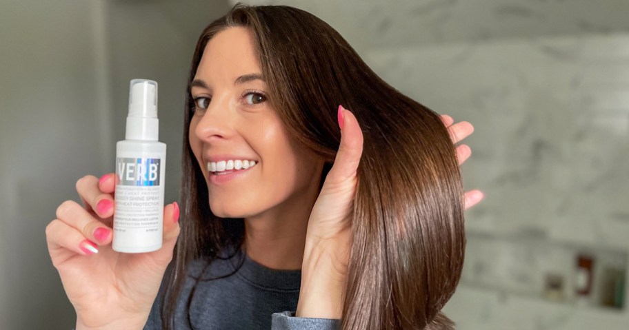 woman holding a bottle of Verb Glossy Shine Spray and showing her shiny brown hair
