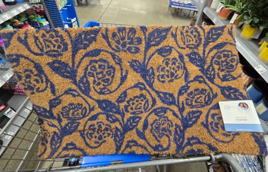 A Walmart cart with a Mainstays by Becky G. & Alejandra Floral Coir Outdoor Mat in it