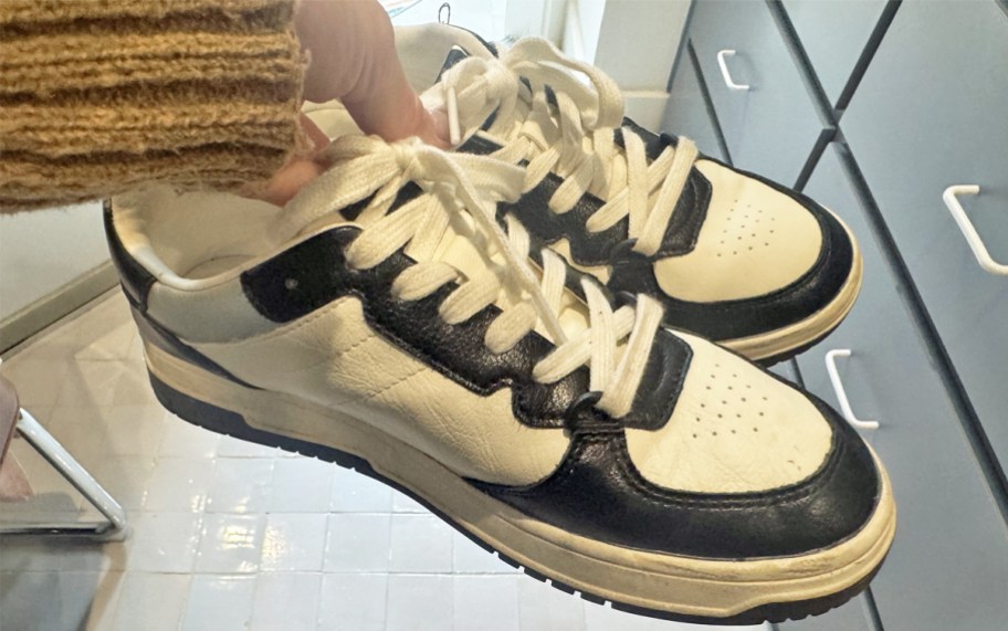 hand holding a pair of white and black sneakers