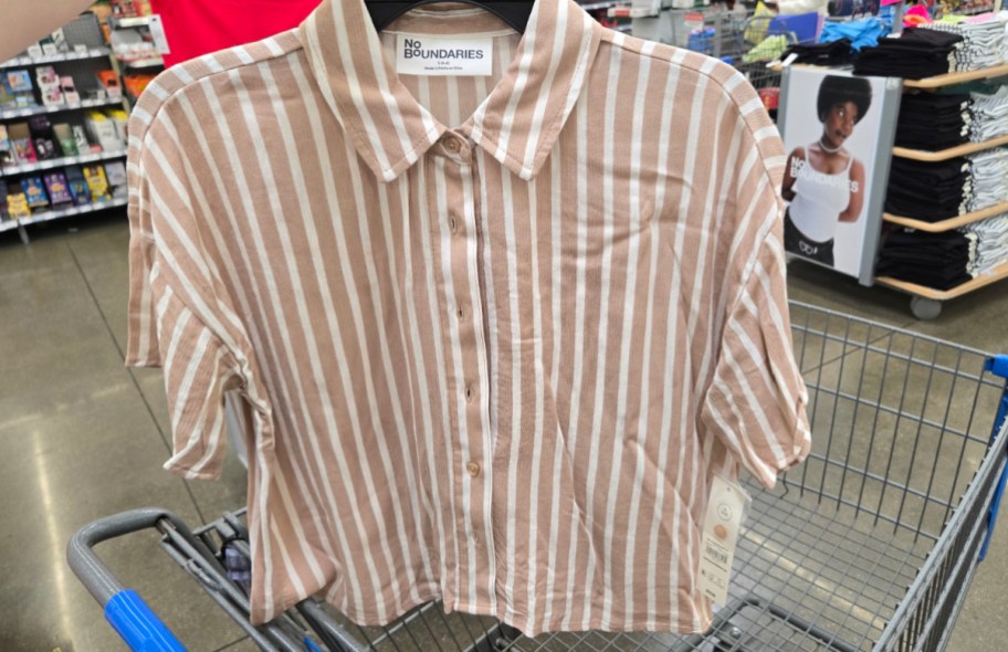 hand holding up shirt set in front of a walmart cart