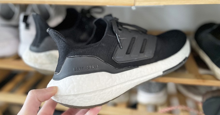 hand grabbing a black adidas ultraboost shoe from shoe rack