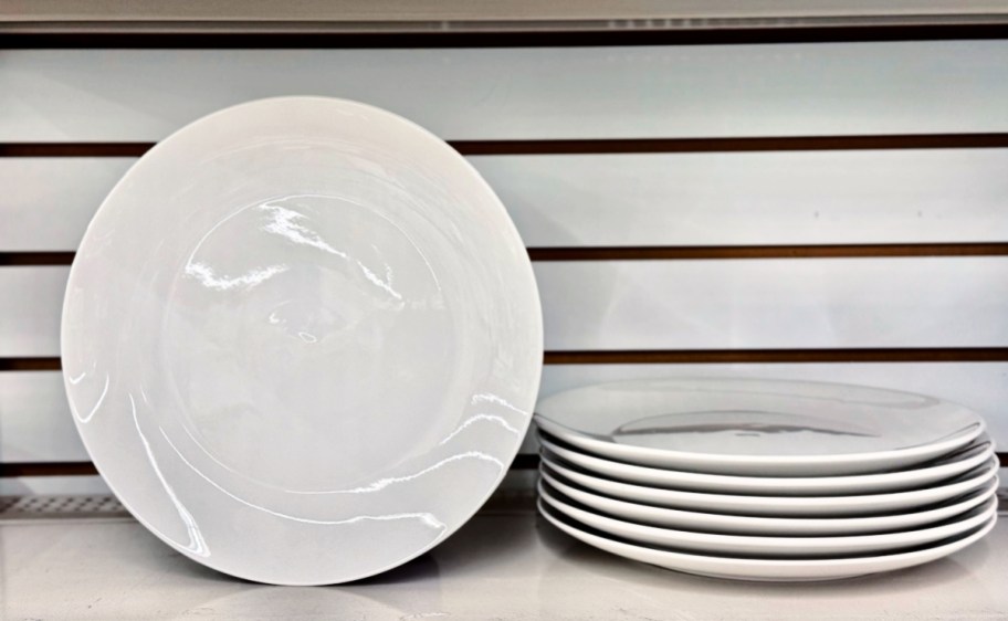 white ceramic plates stacked and standing up next to the stack on a store shelf