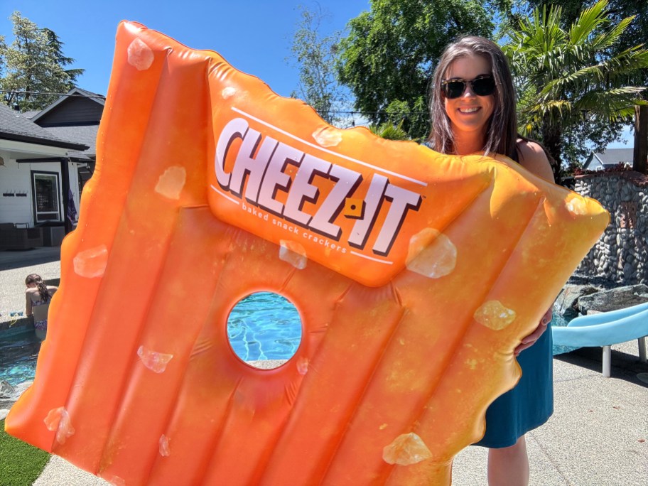 smiling woman standing behind a big orange cheez it shaped pool float