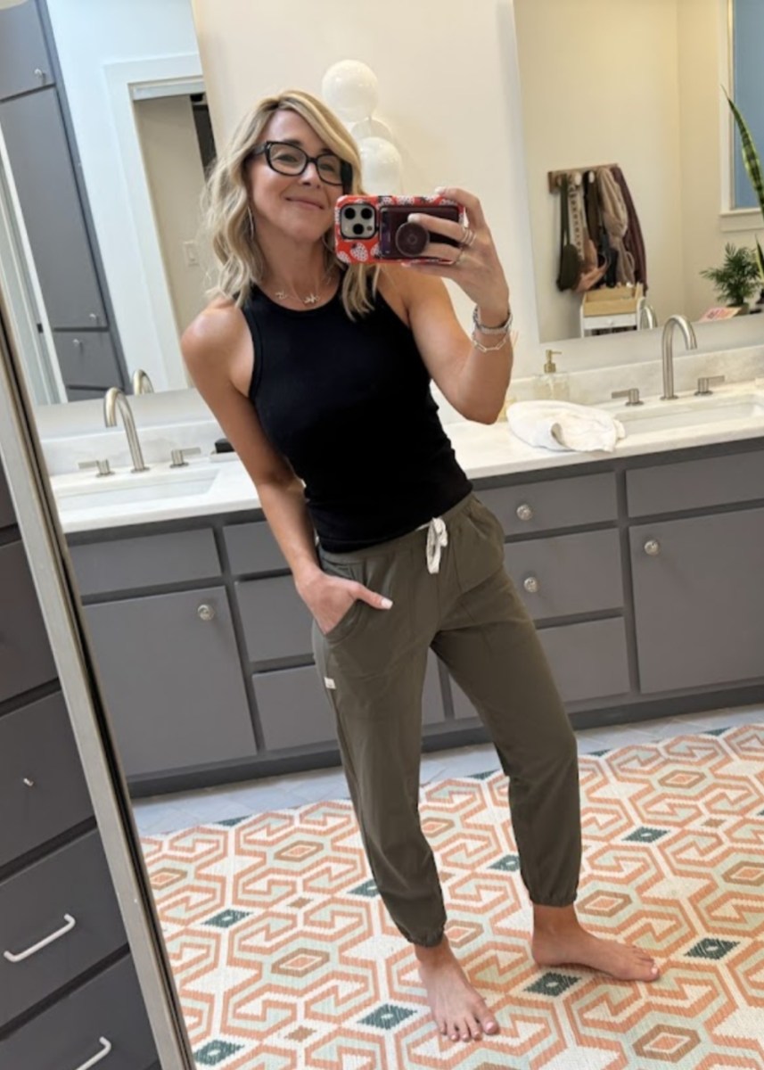 woman taking a selfie wearing a black tank top and green jogger pants