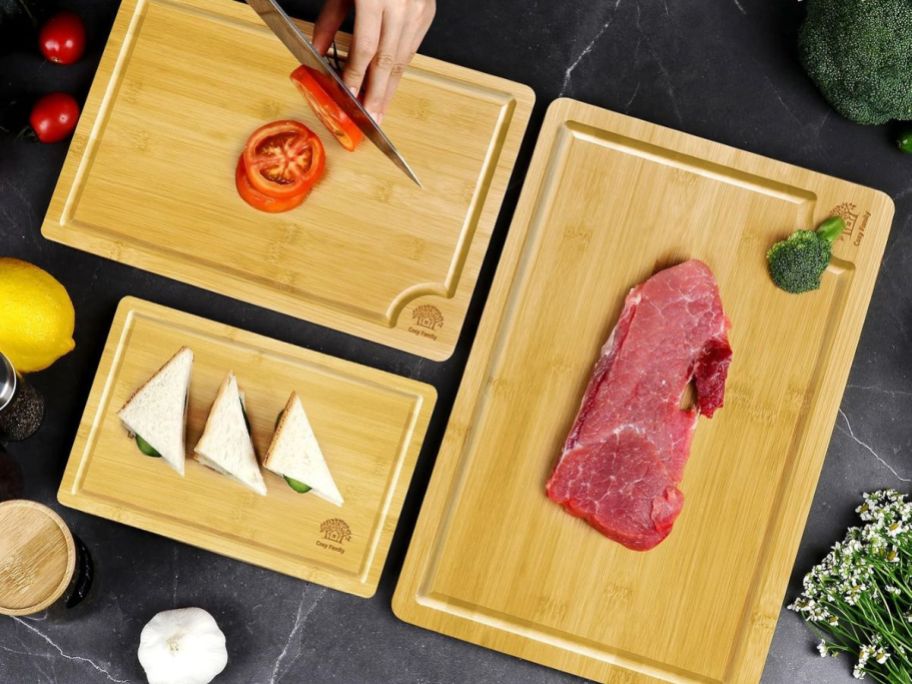 person cutting tomatoes on Cosy Family Bamboo Cutting Board with two other cutting boards next to it with meat and sandwiches on them on counter