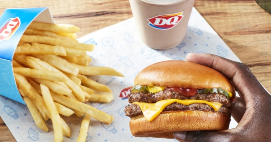 holding a Dairy Queen burger next to fries and a shake