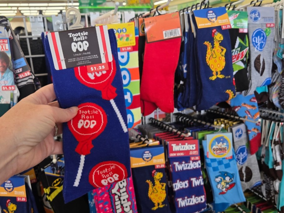 hand holding a pair of Blow Pop socks, more food-themed socks behind it on a store rack
