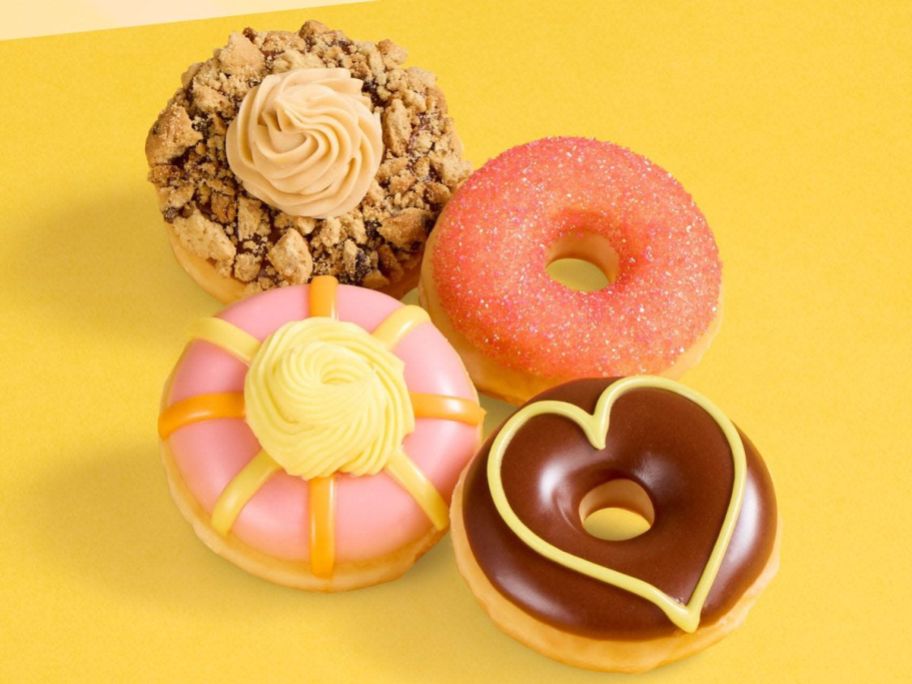 four decorated Krispy Kreme doughnuts on yellow surface