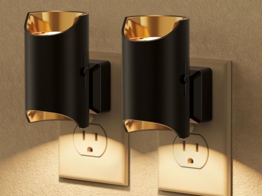 two gold and black night lights in outlet on wall