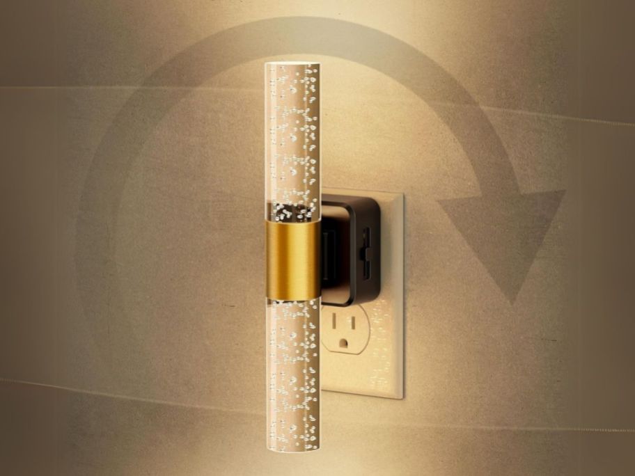 a gold and crystal clear cylinder shaped night light in outlet on wall