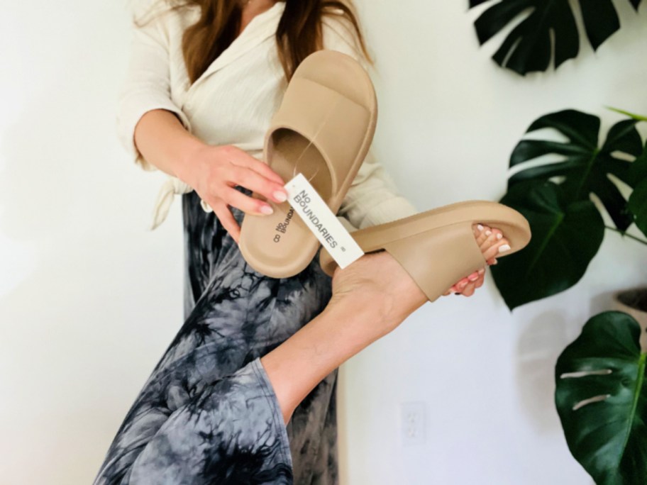 woman wearing a pair of tan slide sandals with her foot lifted and the no boundaries tag showing
