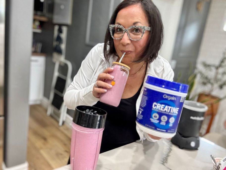woman sipping from smoothie and holding Orgain Creatine Monohydrate Micronized Powder 17.64oz tub in her other hand