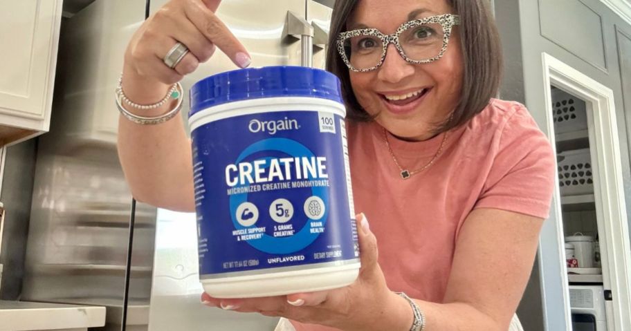 woman holding Orgain Creatine Monohydrate Micronized Powder 17.64oz tub and pointing to it