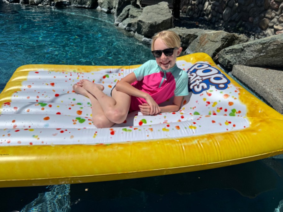 smiling girl laying on a pop tart shaped pool float in a pool