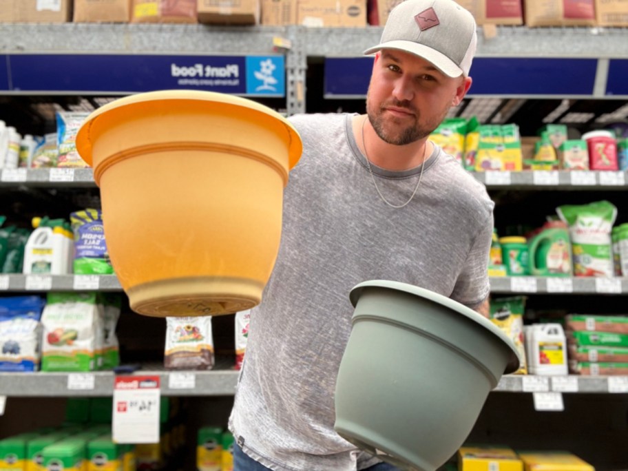 smiling man holding up two self watering plastic planters in a store aisle
