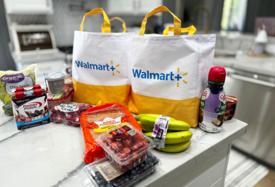 walmart plus grocery delivery bags on a kitchen counter with groceries spread around them