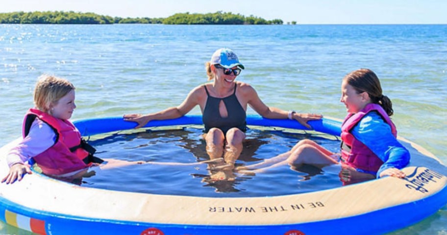 a woman and kids sitting in a large float with a mesh bottom in the ocean