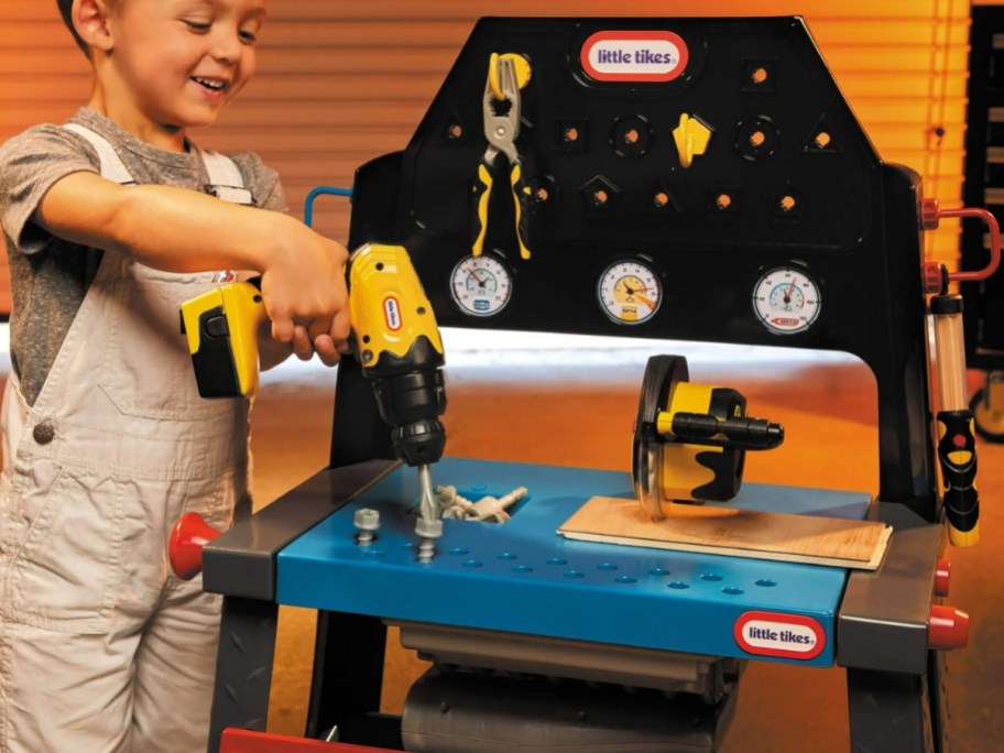 little boy using a toy drill on a Little Tikes wood shop playset