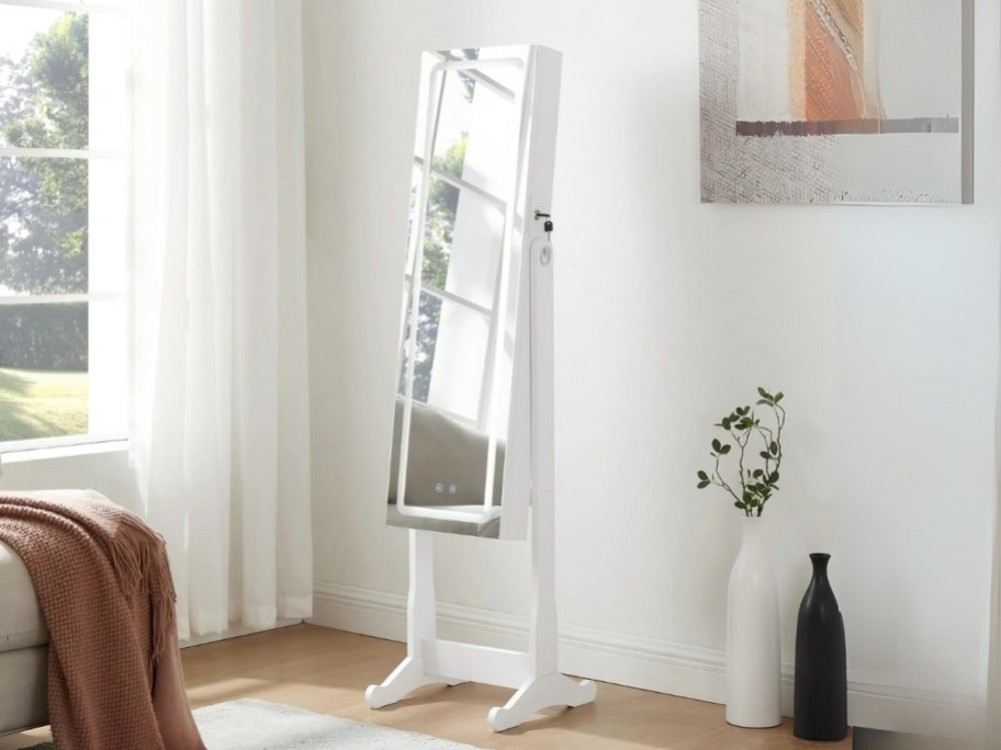a jewelry armoire with a lighted mirror in a bedroom