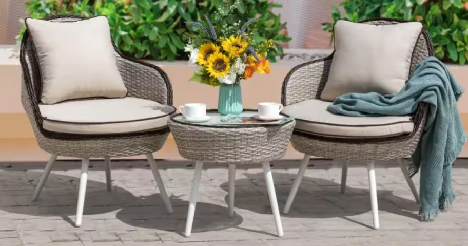 a beige wicker bistro set with cushions on a patio