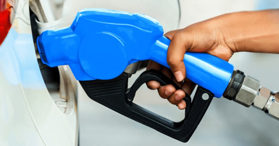 person holding a blue gas pump nozzle in their gas tank