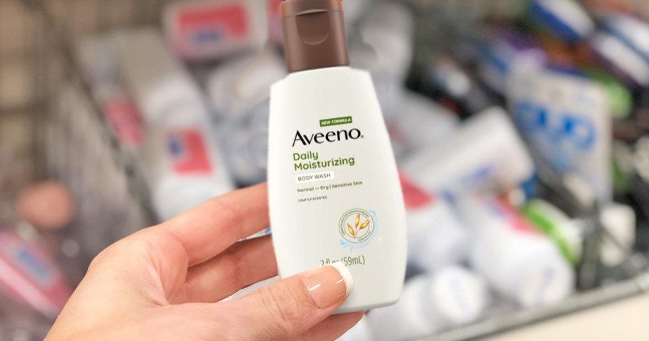 hand holding up a travel-sized bottle of Aveeno Body Wash in store