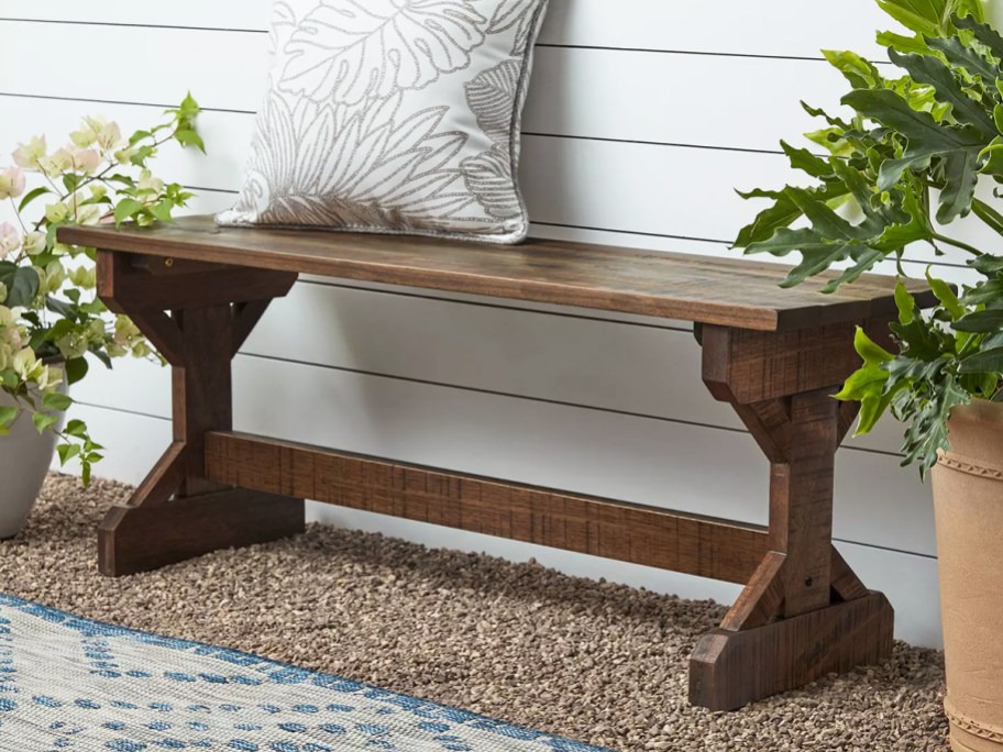 brown wood garden bench with throw pillow on top
